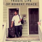 A young man smiles while standing on a porch between two doors, holding a suitcase and duffel bag. The book cover text reads: The Short and Tragic Life of Robert Peace by Jeff Hobbs.